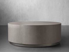 a round concrete table sitting on top of a cement floor next to a white wall