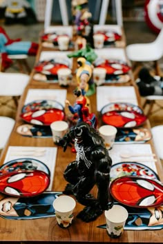 the table is set with red and black plates, silverware, and figurines