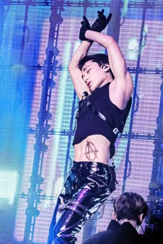 a woman in black top and leather pants on stage with her arms raised above her head