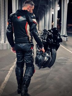 a man in black and red leathers is standing next to a motorbike