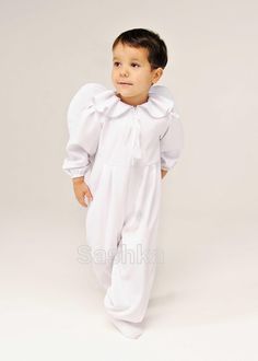 a little boy dressed in white is posing for the camera with his hands on his hips