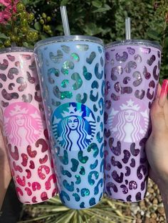 three starbucks tumblers with different designs on them in front of some plants and flowers