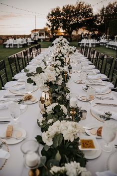 a long table is set with white flowers and plates for an elegant wedding reception at sunset