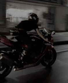 a man riding on the back of a red motorcycle down a city street at night