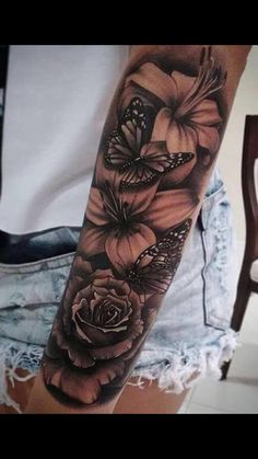 a black and white tattoo with flowers on the arm, butterflies flying over it in the background