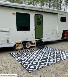 a white trailer parked next to two chairs and a black and white rug on the ground