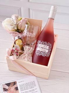 a bottle of wine sitting in a wooden box next to a card and some flowers