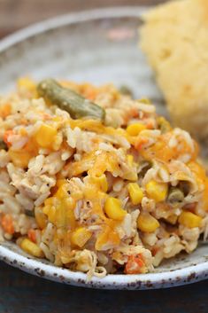 a white plate topped with rice and vegetables next to a piece of bread on top of a table