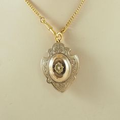 A delightful large antique Victorian gold filled, or "Schaumgold" sentimental shield shaped locket back brooch/pendant in yellow gold tone. With a central tiny seed pearl within a flower head, the petals with a matted finish. This is within an oval mount with beaded edge. To the sides are engraved scrolls. With a hinged locket panel to the reverse with beveled glass. Open the brooch pin to access the locket panel which is easy to open. With a tiny loop for a safety chain. With a simple  brooch f Victorian Filigree Locket Necklace For Anniversary, Victorian Hallmarked Locket Necklace For Anniversary, Victorian Anniversary Locket Necklace Hallmarked, Victorian Pendant Locket Necklace For Anniversary, Victorian Filigree Locket Necklace Collectible, Collectible Victorian Gold Locket Necklace, Vintage Ceremonial Jewelry With Screw Back, Antique Gold Locket Necklace, Historical Gold Medallion Jewelry