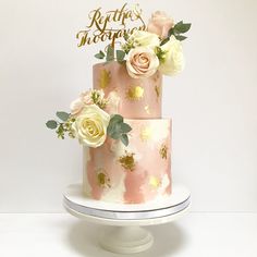 a three tiered pink and gold wedding cake with flowers on top is featured against a white backdrop