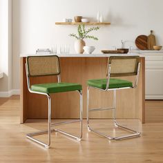 two green chairs sitting on top of a hard wood floor next to a kitchen counter