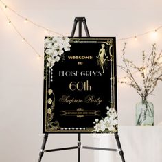 an easel with a welcome sign on it in front of some flowers and lights