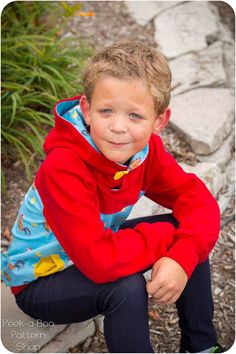 a young boy sitting on the ground with his hands in his pockets and smiling at the camera