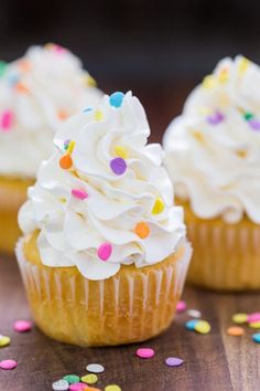 three cupcakes with white frosting and sprinkles on a table