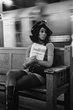 a black and white photo of a woman sitting on a bench with a book in her hand