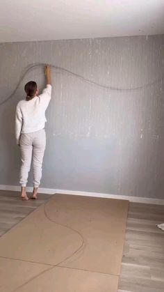 a woman is painting the wall in her living room with gray walls and wood floors