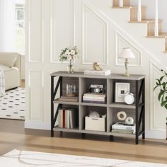 a book shelf with books and magazines on it in front of a stair case next to a couch