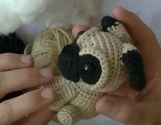 two hands holding a small stuffed animal with yarn in it's mouth and another hand next to it