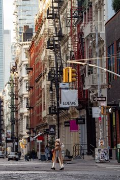 two people crossing the street in front of tall buildings with fire escapes on each side