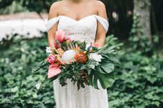 a woman in a white wedding dress holding a bouquet with orange and pink flowers on it