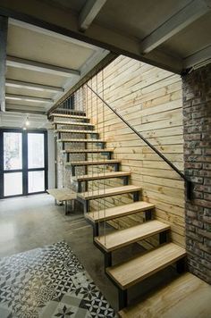 a set of wooden stairs leading up to a brick wall in a room with black and white flooring