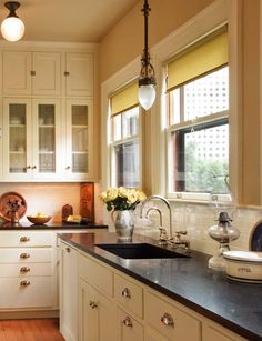 a kitchen with white cabinets and black counter tops next to a window filled with yellow flowers