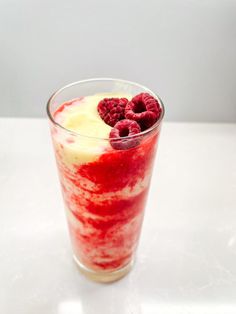 a glass filled with raspberries and cream on top of a white countertop