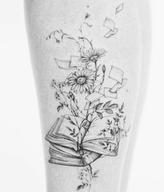 a black and white photo of a book with flowers coming out of it on the thigh