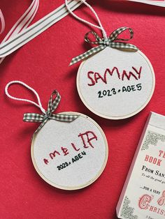 two personalized christmas ornament hanging on a red table with ribbon and book