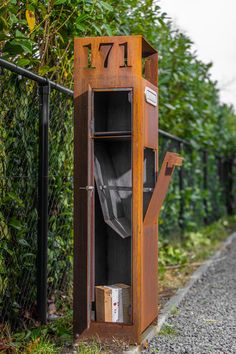 an old wooden cabinet sitting on the side of a road next to a fence and bushes