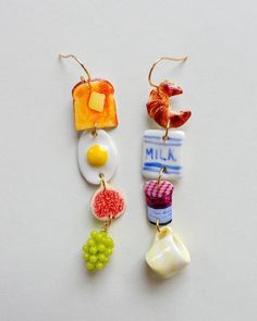 two earrings with different designs on them sitting next to each other and one has a piece of fruit hanging from it's ear wire