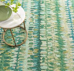 a table with a plant on top of it in front of a green and blue rug