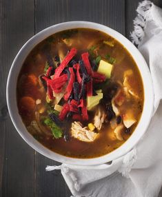 a white bowl filled with chicken tortilla soup on top of a wooden table