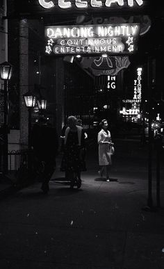 black and white photograph of people walking under a neon sign that reads cellar dancing nighty