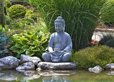 a buddha statue sitting on top of a rock next to a body of water and plants