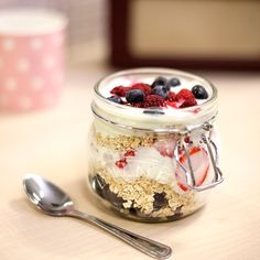 a glass jar filled with granola, berries and yogurt next to a spoon