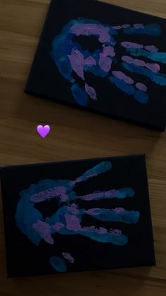 two handprints on black paper with a pink heart in the middle and purple hands