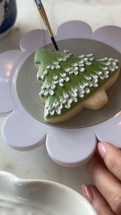 a cookie decorated like a christmas tree on a plate with a brush in its hand