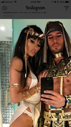 a man and woman dressed up in egyptian garb posing for a selfie on their cell phone