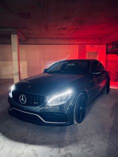 a black car is parked in an empty parking garage with red light coming from behind it