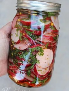 a hand holding a mason jar filled with pickled radishes and other veggies