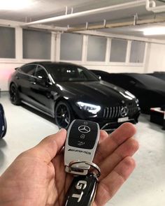 a hand holding a car key in front of several other cars parked in a garage