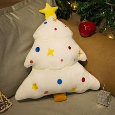 a white christmas tree pillow sitting on top of a couch next to a christmas tree