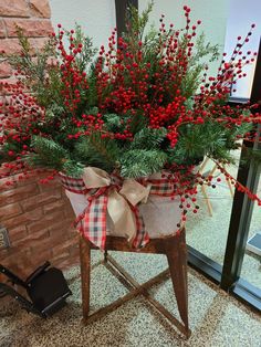 a potted plant sitting on top of a wooden stand with red berries and greenery