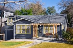 a small gray house with yellow trim on the front and side windows, covered by wooden slats