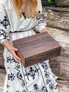 a woman in a white dress holding a wooden box with the words wedding day engraved on it