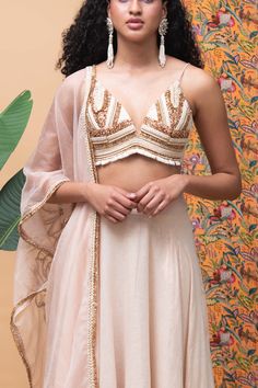 Editor's Note The fully embroidered panel blouse with a deep v-neck comes in with a rose gold lehenga along with a rose gold embroidered dupatta. Color: Rose gold Fabric: Cotton Occasion: Festive and Wedding Guest Components: Lehenga, blouse and dupatta Disclaimer: Product color may slightly vary due to photographic lighting sources or your monitor setting. Care: Dry Clean Only About the Designer Rishi & Vibhuti label combines traditional elements with modern aesthetic uniquely to create chic oc Festive V-neck Lehenga With Dupatta, Wedding Choli With Zari Work And V-neck, Elegant V-neck Lehenga With Zari Work, Festive V-neck Lehenga With Zari Work, Gold Palazzo Set For Wedding, Fitted Gold Palazzo Set With Intricate Embroidery, Gold Palazzo Set For Wedding Party, Elegant V-neck Lehenga With Resham Embroidery, Elegant Lehenga With Resham Embroidery And V-neck