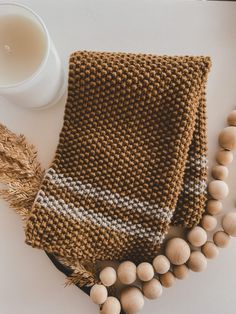 a knitted brown scarf next to some beads and a glass of milk on a white surface