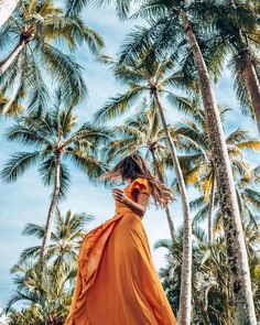 a woman in an orange dress standing among palm trees