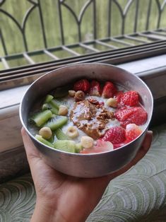 a person is holding a bowl of cereal with fruit and nuts in it while looking out the window